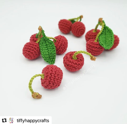 A cluster of red, crochet amigurumi style cherries on a plain white background with a re-gram symbol on the bottom left corner with the original creators social media handle; @tiffyhappycrafts