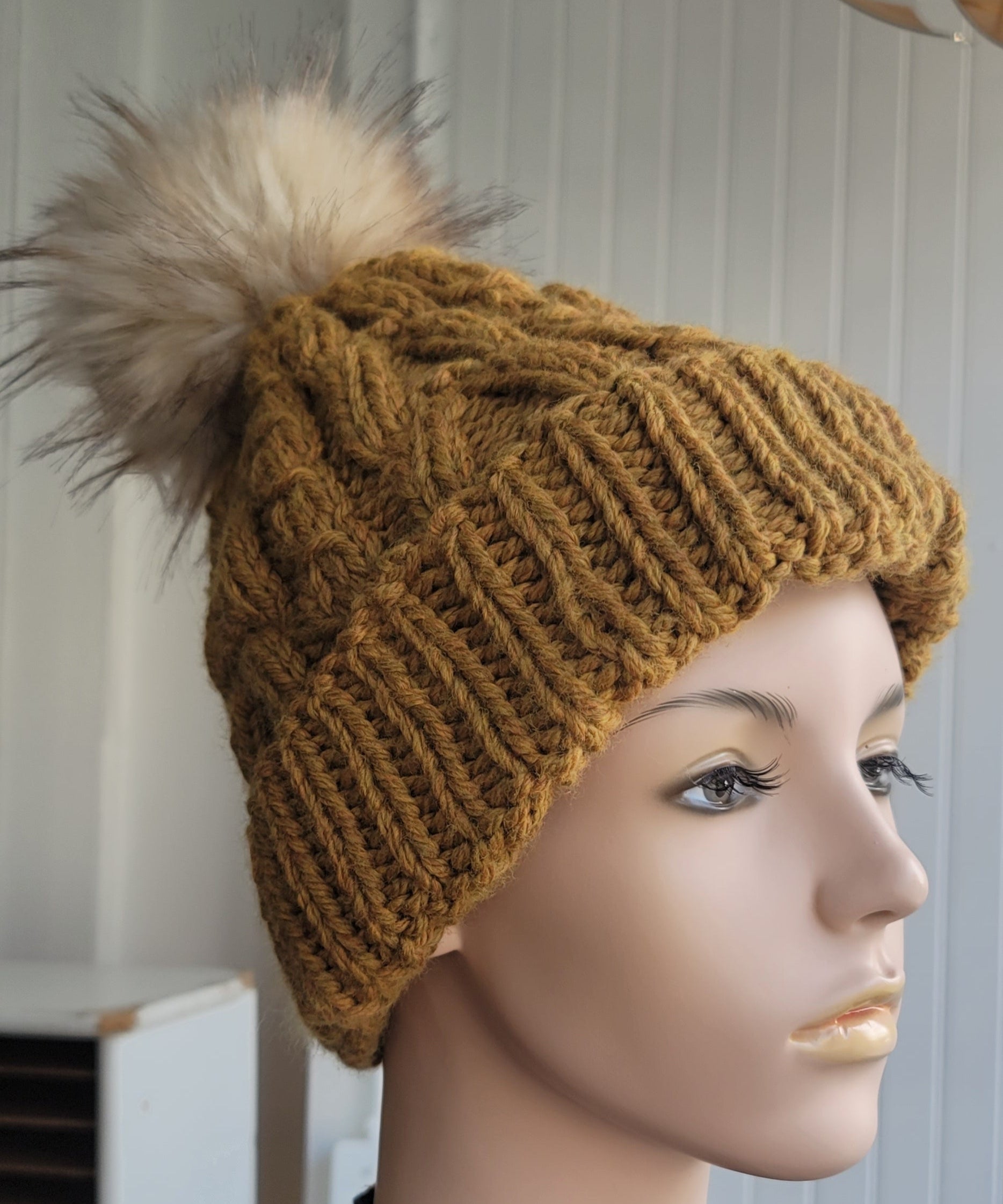 Mannequin head wearing a mustard yellow knitted hat with a pom-pom on a white background