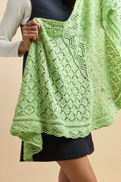 Green knitted garment held by a person against a beige background