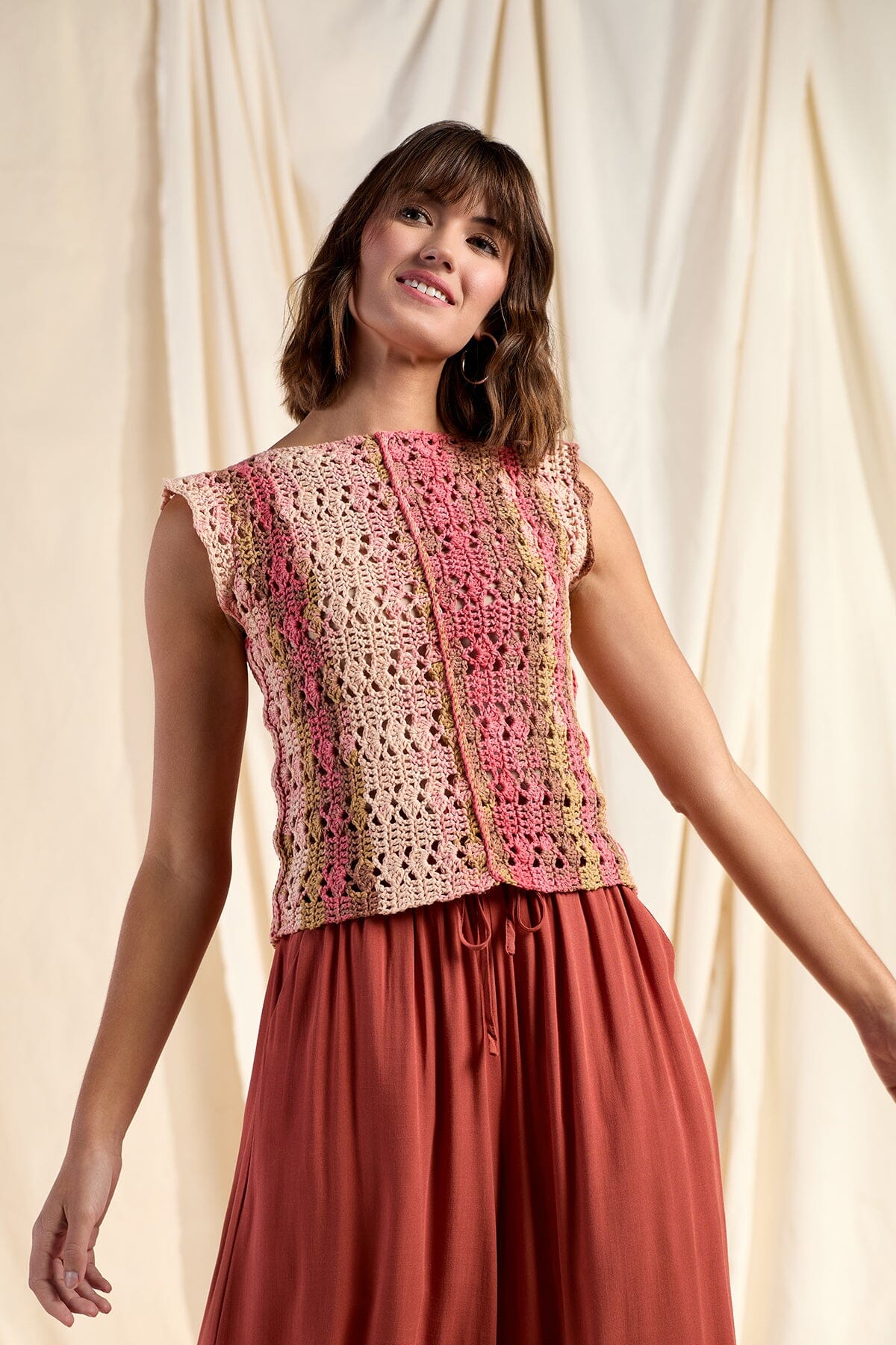 Woman wearing a colorful crochet top and red skirt against a beige curtain background