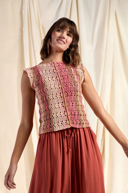 Woman wearing a colorful crochet top and red skirt against a beige curtain background