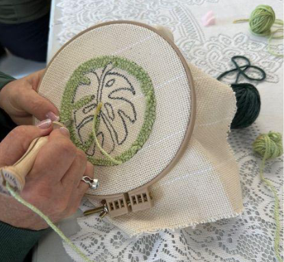 Person embroiderying a leaf design on a hoop with green thread.