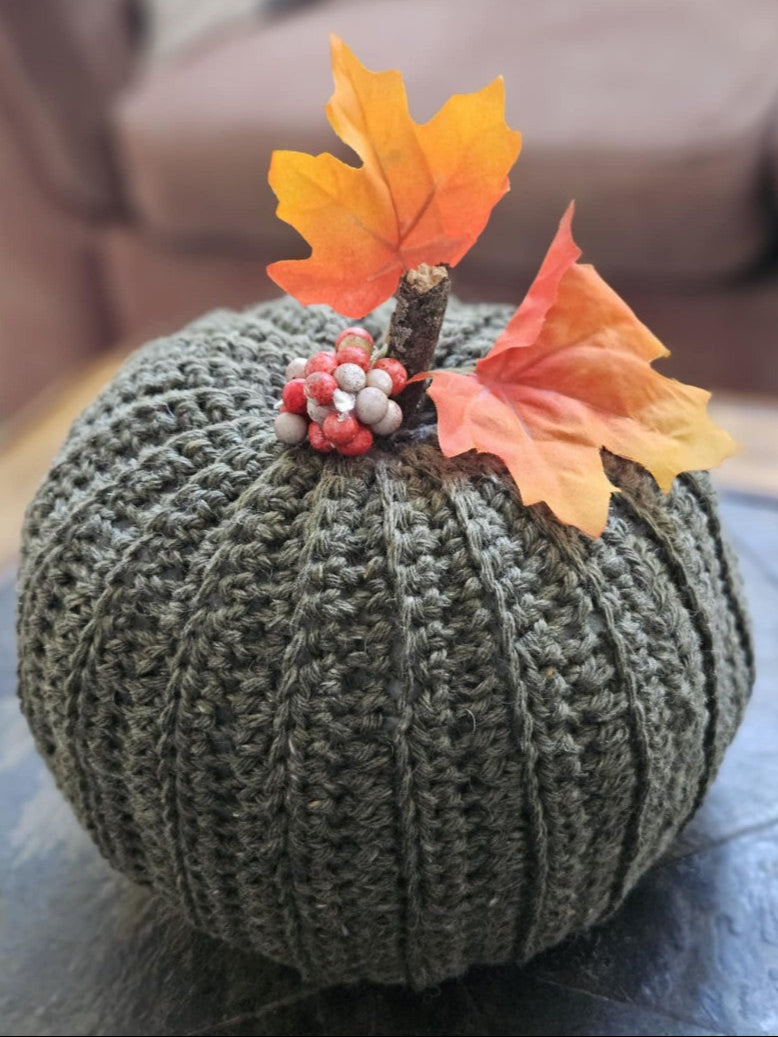 Crocheted pumpkin with autumn leaves and berries on a neutral background
