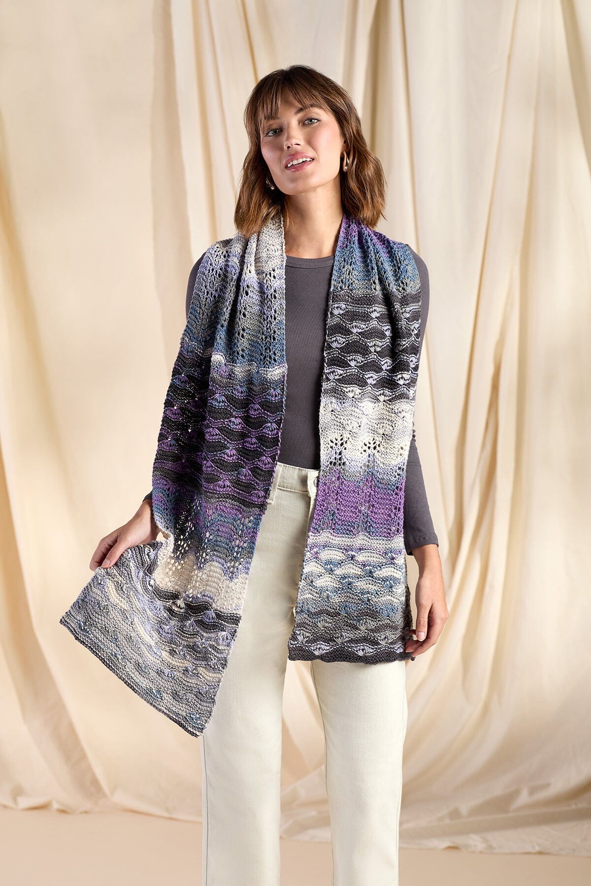 Woman wearing a long, patterned scarf against a beige curtain background