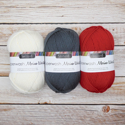 Three balls of Estelle Superwash Merino Wool yarn in white, gray, and red on a wooden surface.