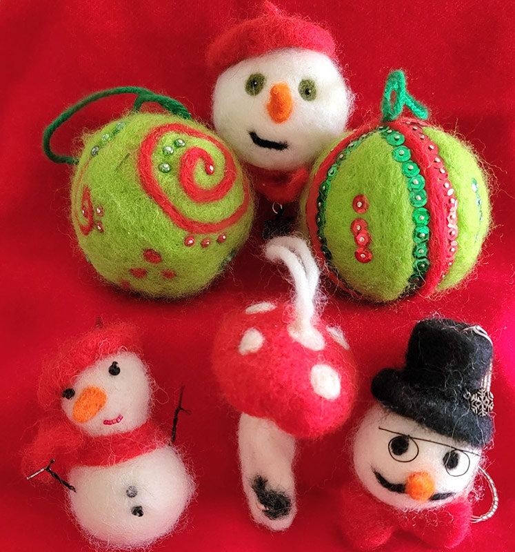 A variety of needle felted winter/Christmas decorations including a green and red spiral, a red and white snowman, a green mushroom, and a snowy scene with a Christmas tree and ornaments.
