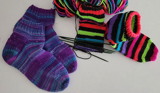 A photo of two pairs of knit socks, one complete, the other held on double pointed needles.
