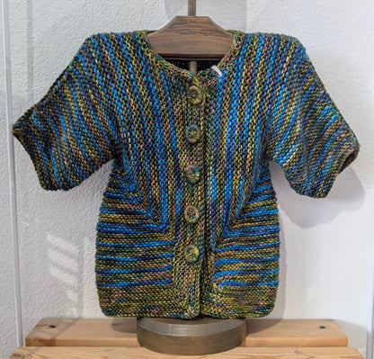 Knitted sweater on a mannequin against a white wall with wooden shelves below.